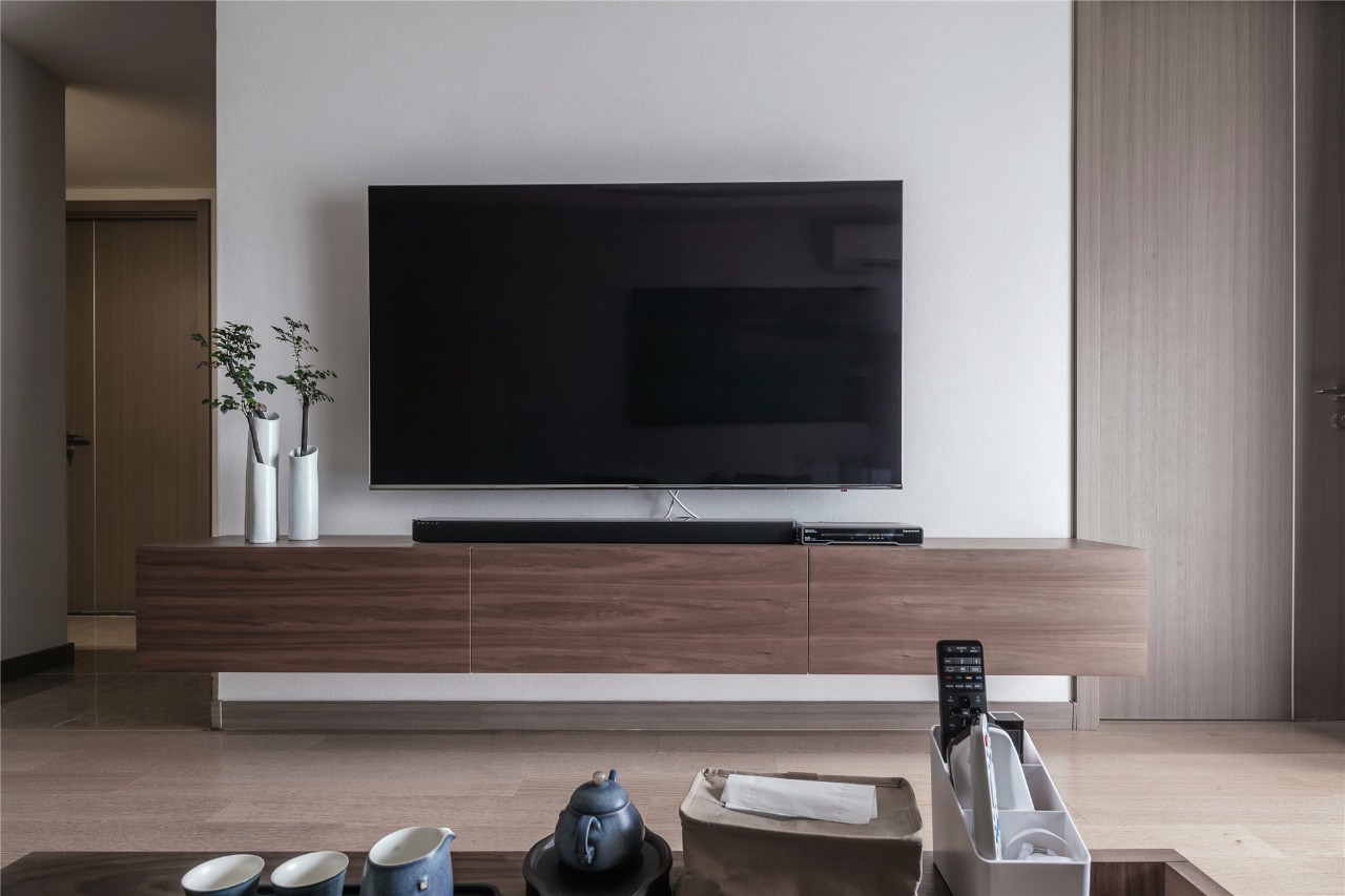 电视背景墙简约而利落,木质电视柜悬空而置,摆放极简花瓶与绿植,带来