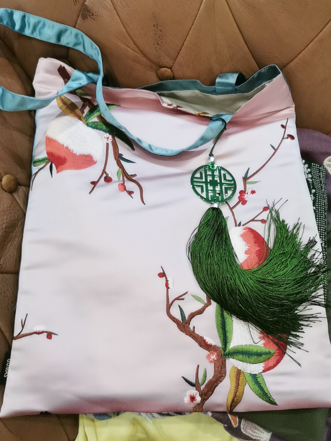 Hand-embroidered botanical silk pouch showing detailed red peach blossom and green leaf work